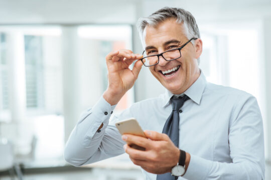 Direttore della PMI guarda il telefono sorridendo della gestione aziendale.