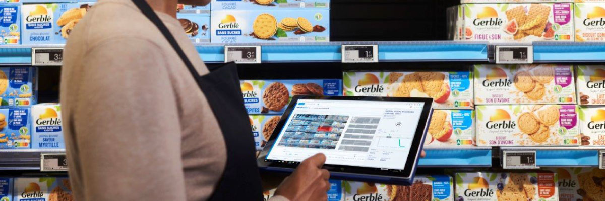 Addetta al supermercato aggiorna le etichette elettroniche davanti ad uno scaffale di biscotti, con un tablet